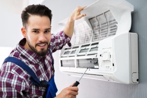 Happy Male Technician Repairing Air Conditioner With Screwdriver